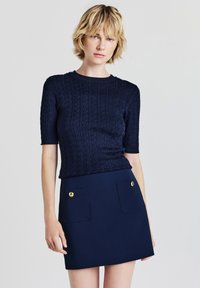 Dunkelblauer gestrickter Pullover mit kurzen Ärmeln und einem strukturierten Muster, kombiniert mit einem passenden Minirock, der zwei Fronttaschen und goldene Akzente aufweist.