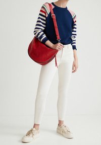 Donkerblauwe trui met gestreepte mouwen, witte spijkerbroek en beige sneakers. Rode leren handtas met reliëfpatroon. Casual outfit.