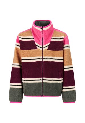 Junge Person, die eine gestreifte Fleecejacke, dunkle weite Hosen und schwarze Sneakers mit weißen Sohlen und Schnürsenkeln trägt.