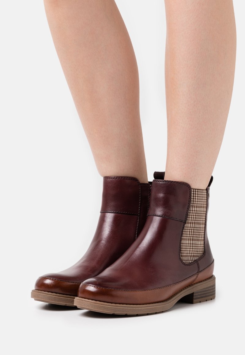 Bottines en cuir marron avec des panneaux élastiques sur les côtés, des accents de plaid texturé, des semelles en caoutchouc marron et une pointe arrondie.