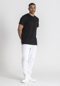 Czarna, strukturalna koszulka z krótkim rękawem, w połączeniu z białymi, dopasowanymi dżinsami i białymi snekerami, na manekinie na neutralnym tle.