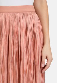 Gonna plissettata rosa con superficie texturizzata e elastico in vita. Presenta pieghe verticali su tutta la lunghezza, creando una silhouette fluida.