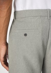 Graue, strukturierte Hose mit einer Gesäßtasche, die mit einem schwarzen Knopf versehen ist. Der Bund ist sauber verarbeitet und präsentiert ein modernes, maßgeschneidertes Design.