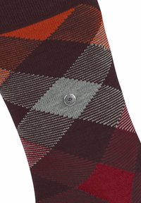 Chaussette tricotée arborant un motif argyle dans des tons de bordeaux, gris, rouge et orange, avec un logo métallique circulaire sur le côté.