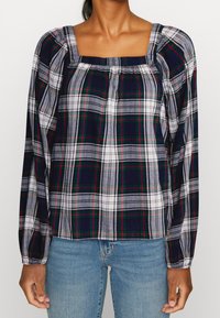 Chemisier à manches longues à carreaux bleu marine, blanc et vert. Il présente un col carré, des détails froncés et un tissu doux et léger.