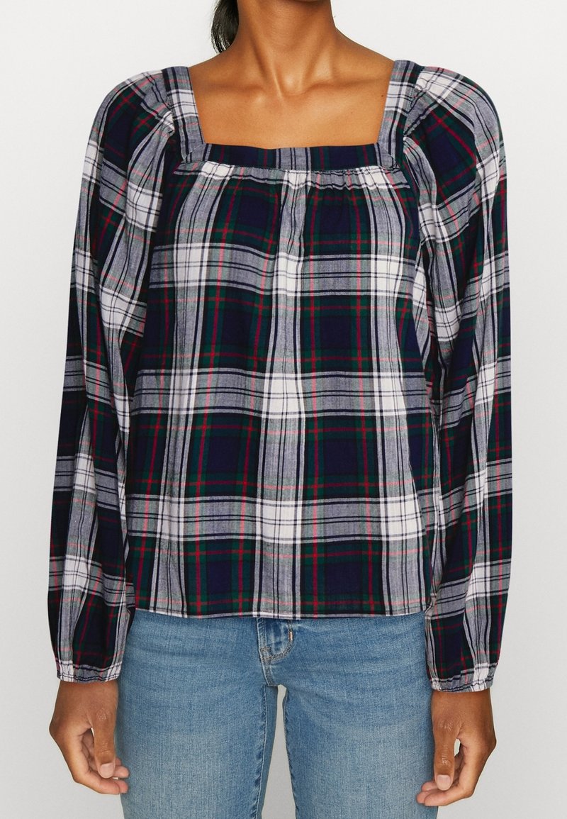 Chemisier à manches longues à carreaux bleu marine, blanc et vert. Il présente un col carré, des détails froncés et un tissu doux et léger.