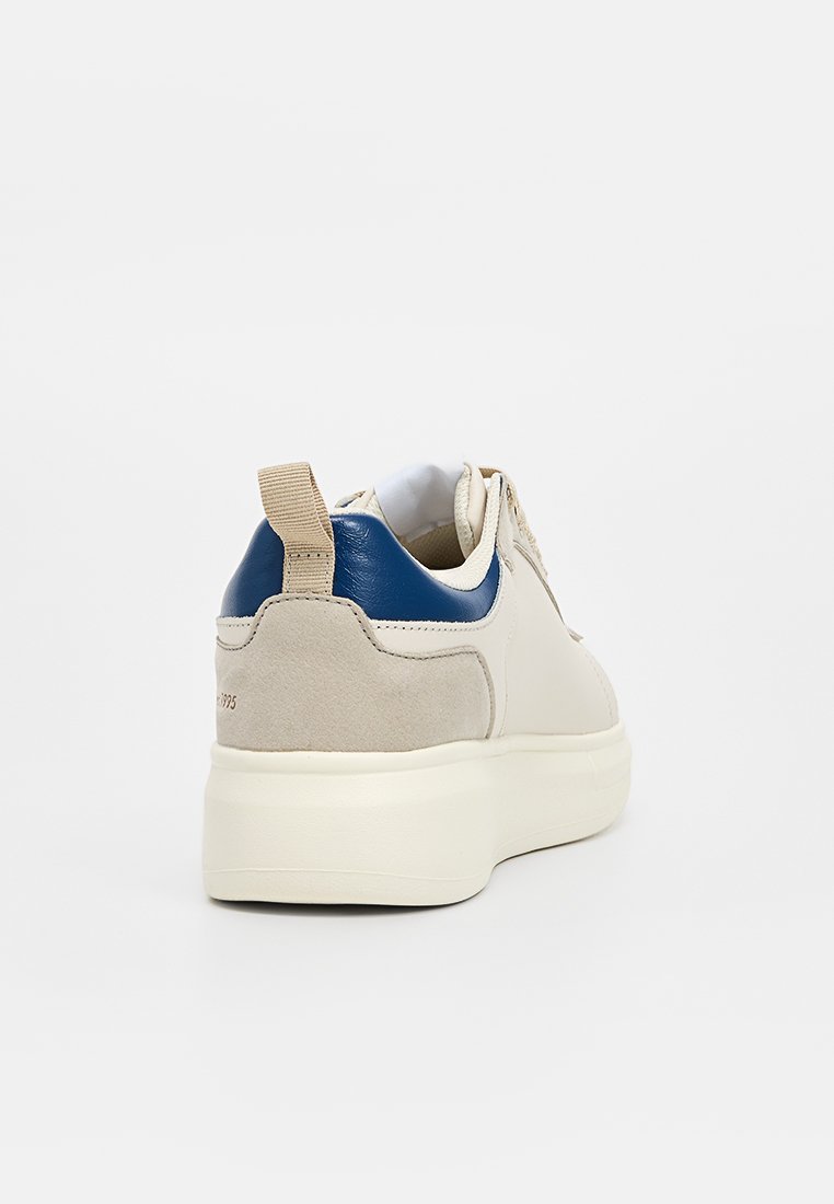 Sneaker beige con accenti in pelle blu, parte posteriore in suede, linguetta imbottita e linguetta per il tallone. Suola bianca spessa con superficie texturizzata.