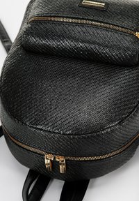 Schwarzer, strukturierten Kunstleder-Rucksack in runder Form, mit goldenen Reißverschlussakzenten und einer Vorderasche. Glatte Träger sind zum Tragen angebracht.