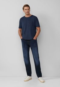 Navyblauwe katoenen T-shirt met een borstzak, gecombineerd met donkere spijkerbroek en witte sneakers, wat zorgt voor een casual look. Gladde textuur en eenvoudig ontwerp.