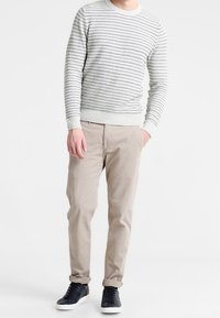 Grårandig stickad tröja med rundad halsringning, i kombination med beige byxor och marinblå sneakers. Avslappnad passform med ribbade detaljer.