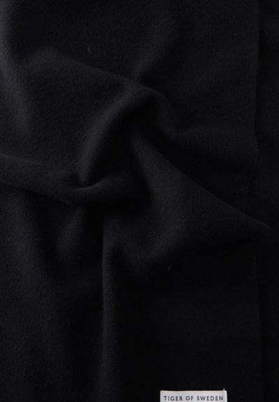Μαύρο ύφασμα με απαλές πτυχές και μια μικρή λευκή ετικέτα που γράφει "Tiger of Sweden" στην κάτω δεξιά γωνία.
