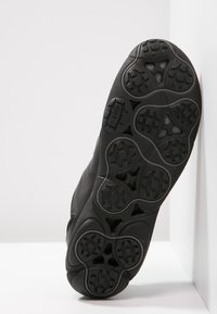 Black athletic shoe sole with circular and rectangular traction patterns, textured rubber, and “GEOX” branding embedded in the design.