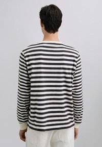 Cămașă cu mânecă lungă, cu un design în dungi alb-negru. Fabricată dintr-un material moale, aceasta are un decolteu rotund și manșete ribbate.