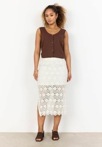 Top sans manches marron avec des boutons, associé à une jupe midi blanche à motif en dentelle avec un ourlet festonné. Des sandales à glissière marron complètent le look.