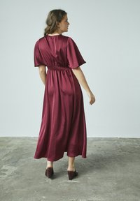 Burgundy satängmaxikjol med korta, breda ärmar, rynkad midja och en flödande kjol. Matchad med bruna klacksandaler.