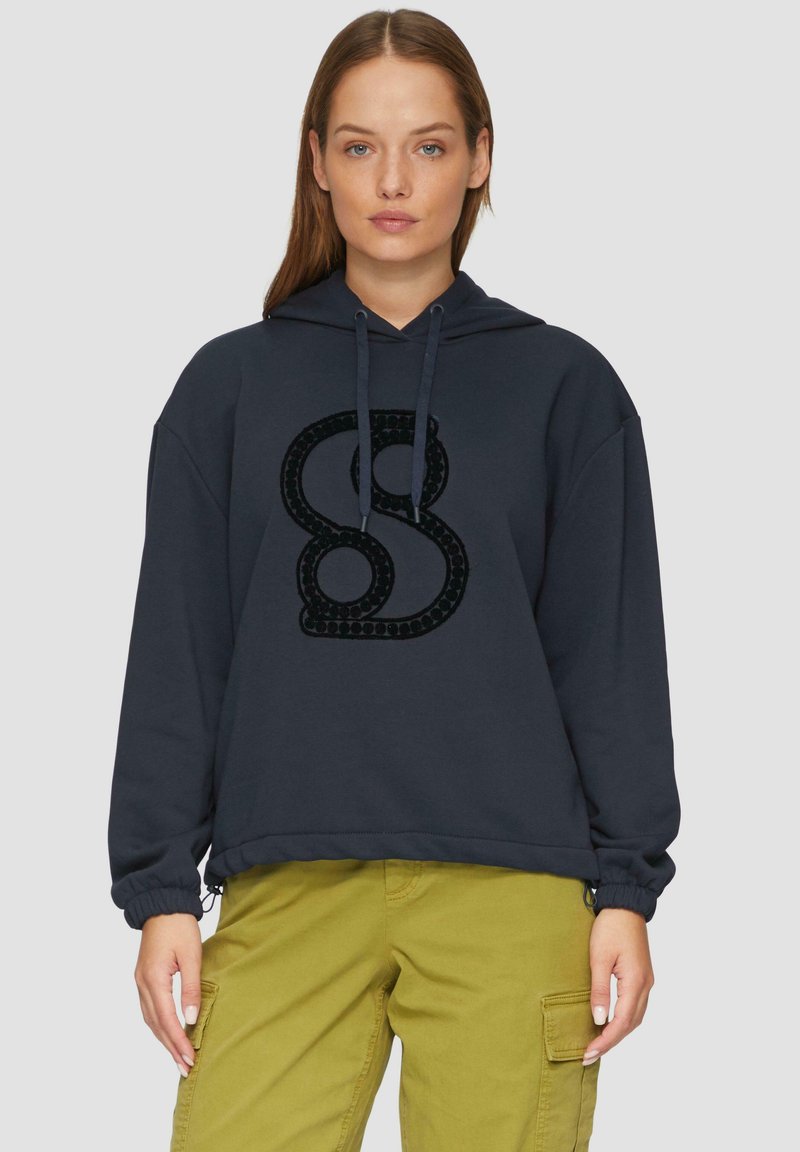 Haut à capuche bleu foncé avec cordon, présentant un design en relief de couleur noire en forme de "S" sur le devant et des poignets élastiques. Coupe décontractée.