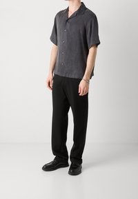Camisa de manga corta de color gris anhídrido con un corte relajado, cuello y cierre de botones, combinada con pantalones negros y zapatos de vestir de cuero.