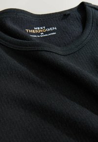 Czarna termiczna koszulka z okrągłym dekoltem, prążkowaną fakturą i widoczną metką z napisem "NEXT THERMOGEN M MADE IN BANGLADESH".