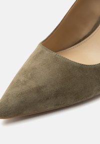 Chaussure plate en daim beige à bout pointu, intérieur en cuir marron lisse et couture propre le long du bord.