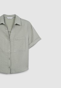 Camicia a maniche corte con bottoni di colore verde chiaro, con un tessuto strutturato, colletto alla francese e un'unica tasca sul petto.