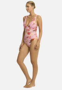 Jednoczęściowy kostium kąpielowy w kolorze różowym z kwiatowym wzorem. Posiada głęboki dekolt w kształcie litery V, szerokie ramiączka oraz dopasowany krój z teksturowanym pasem.
