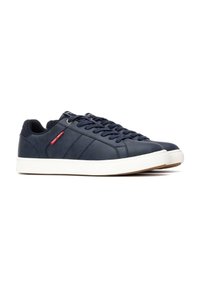 Baskets bleu marine en cuir texturé, avec une semelle en caoutchouc blanc, un laçage à l'avant et une étiquette de marque rouge sur le côté.