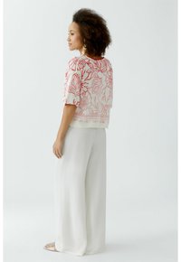 Witte top met rood bloemenpatroon, losse pasvorm, korte mouwen; gecombineerd met wijde witte broek, soepel materiaal, en open teen sandalen.