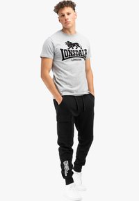 Grå bomullströja med svart Lonsdale London-logotyp, matchad med svarta cargo sweatpants med sidofickor och vita varumärkesdetaljer.