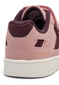 Różowe zamszowe sneakersy z ciemniejszymi burgundowymi akcentami i panelami z siateczki. Oferują strukturalną białą gumową podeszwę oraz wytłoczone logo na pięcie.