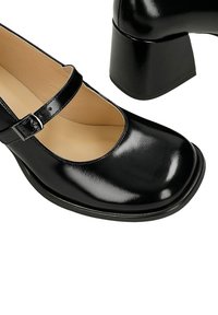 Czarne lakierowane buty Mary Jane z okrągłym noskiem, regulowanym paskiem wokół kostki oraz szerokim, prostokątnym obcasem. Gładka tekstura i błyszczące wykończenie.