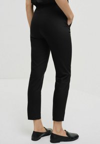 Czarne dopasowane spodnie o prostym kroju, z umiarkowanym stanem, bocznymi kieszeniami i gładką fakturą. Połączone z czarnymi płaskimi butami.
