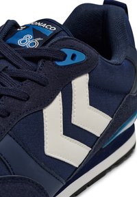 Marinblå sneakers med vita zigzag-accenter, som har en texturerad ovandel i tyg, mjuka inslag av mocka och blå detaljer på öglorna.