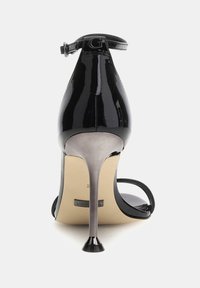 Černé lakované kožené sandály na vysokém podpatku s nastavitelným pásem kolem kotníku, špičatou špičkou a metalickým jehlovým podpatkem. Hladký, lesklý povrch.