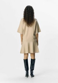 Beige strikkjole med korte ærmer, flared kant og struktureret finish, parret med knæhøje sorte læderstøvler.