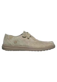 Zapatos de lona beige con punta redondeada, superficie texturizada y suela de goma de perfil bajo. Presentan cordones decorativos y un detalle de logo en el lateral.