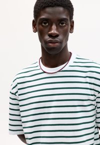 Tricou cu mânecă scurtă, în dungi alb și verde închis, cu guler rotund și un croi lejer. Purtați cu o simplă colier din mărgele.