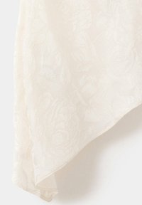Tissu blanc avec un motif floral en relief de rose et une texture douce et drapée visible sur le bord.