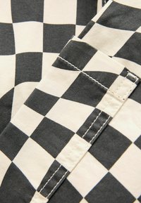 Black and white checkered fabric featuring a cotton texture, with visible stitching on a folded edge. Clear alternating squares pattern.