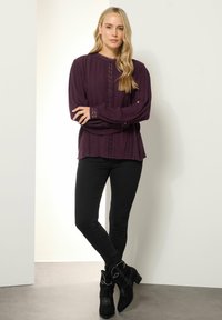 Blusa lunga viola a maniche lunghe con strisce verticali testurizzate e dettagli in pizzo, abbinata a jeans skinny neri e stivali alla caviglia neri con particolari.