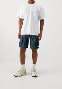 Vit bomulls t-shirt, lös passform, parat med mörkblå cargoshorts med flera fickor och lättviktsmaterial. Grå träningsskor med detaljer.