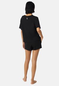 Czarny bawełniany T-shirt z krótkim rękawem o luźnym kroju, zestawiony z czarnymi szortami. Charakteryzuje się minimalistycznym logowaniem z tyłu. Gładka tekstura.