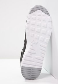 Svart sneakersula med en texturerad vit gummiunderlag. Har ett diamantsmönster och framträdande spår för grepp. Nike-logotyp prägling.