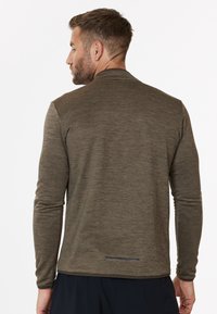 Langarm-Sportshirt aus strukturiertem olivgrünen Stoff, mit hohem Kragen, Daumenlöchern und reflektierenden Details am Saum.
