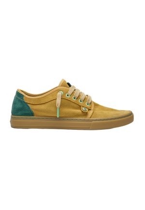 Zapatilla casual de corte bajo con cuerpo de ante color mostaza, talón de ante verde, cordones beige y suela de goma marrón claro.