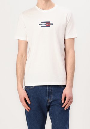 Biała bawełniana koszulka z krótkimi rękawami, z nadrukowanym logo w granatowo-czerwonych prostokątach na środku klatki piersiowej. Casualowy, regularny krój.