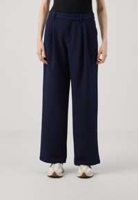 Navy wide-leg trousers with pleats, made of soft fabric. Features a high waistband and pockets, paired with light-colored sneakers.