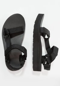 Black sandals with a textured sole, featuring adjustable nylon straps. They have a flat, cushioned platform for comfort.