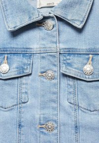 Giacca in denim azzurro chiaro con bottoni in metallo argentato, due tasche sul petto, cuciture visibili e un design classico del colletto.