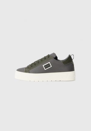 Sneaker grigia con superiore testurizzato, dettagli verde oliva, suola bianca, design classico con lacci e un logo rettangolare sul lato.