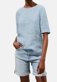 Ljusblå, texturerad kortärmad skjorta med rund halsringning, parat med ljusa jeansshorts som har upprullade ärmslut och sidofickor.